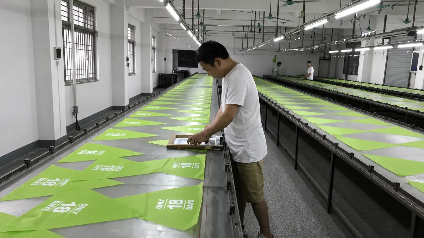 伞厂工人在定制雨伞伞片上进行企业 Logo 丝网印刷