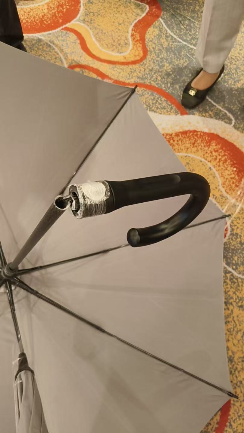撑开的灰色雨伞,黑色弯柄与中棒连接处断裂分离